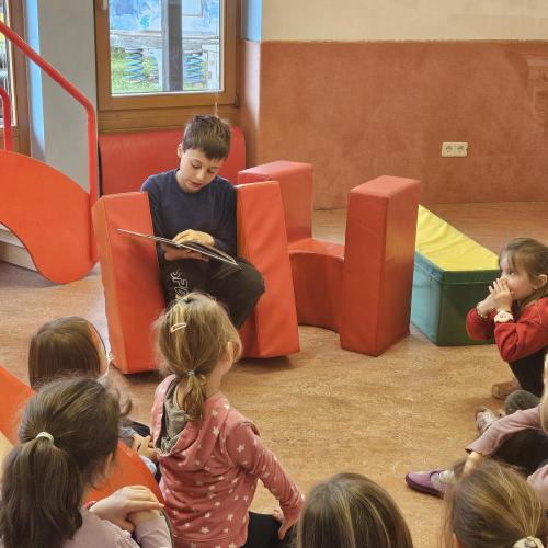 Junge liest Kindern im Kreis aus seinem Buch vor