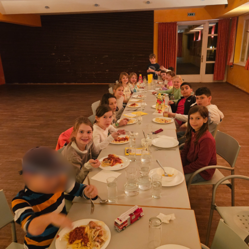 Kinder sitzen an langer Tafel und essen zu Abend