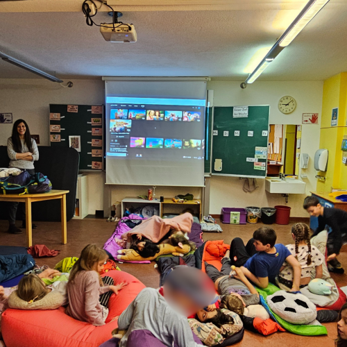 Kinder liegen in Schlafsäcken und schauen nach vorne zum Beamer wo ein Film läuft