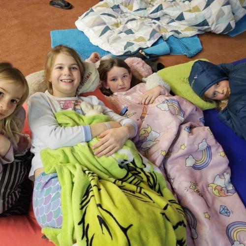 Vier Mädchen liegen am Boden unter Decken und im Schlafsack
