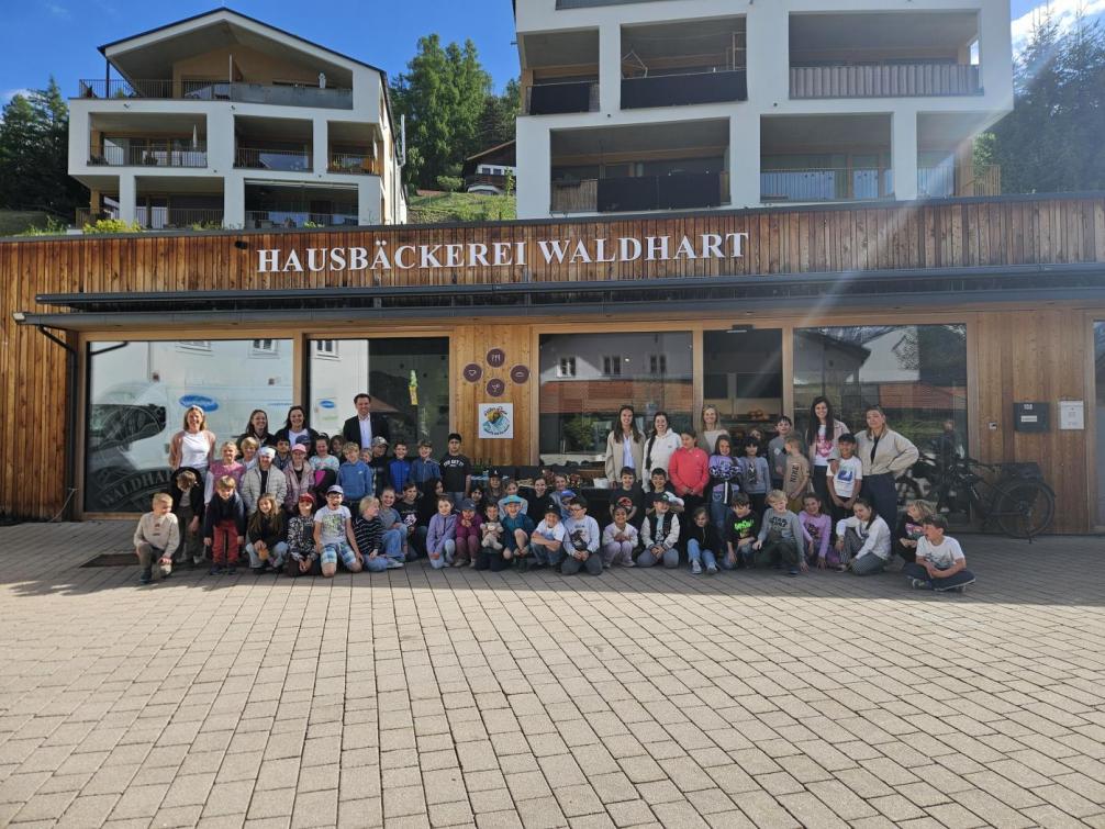 Kinder der Schule gemeinsam mit Lehrerinnen und Bürgermeister vor der Bäckerei 
