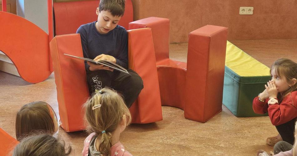 Junge liest Kindern im Kreis aus seinem Buch vor