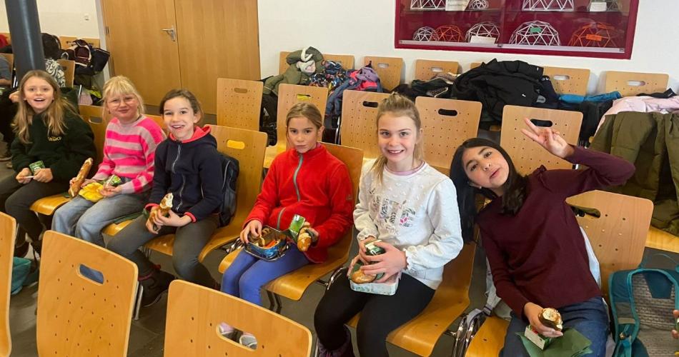 Kinder sitzen auf Stühlen und jausnen