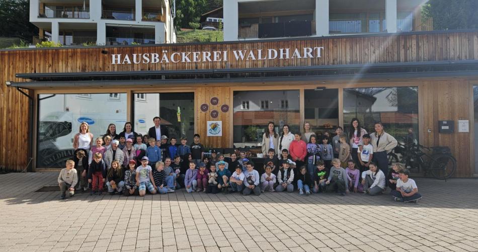 Kinder der Schule gemeinsam mit Lehrerinnen und Bürgermeister vor der Bäckerei 